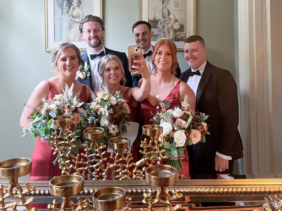 Bridal party taking a group selfie using a mirror at wedding venue